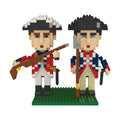 Two soldier figures from the Revolutionary War Soldiers Mini Blocks set stand on a green baseplate, dressed in 18th-century uniforms—one in a red coat with a rifle, the other in blue with a staff.
