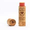A bamboo tube of Cherry Lip Balm with its cap off, engraved with a bee and heart. The cap reads "Door County Cherry Handmade" beside a cherry illustration, showcasing natural beeswax and moisturizing oils.
