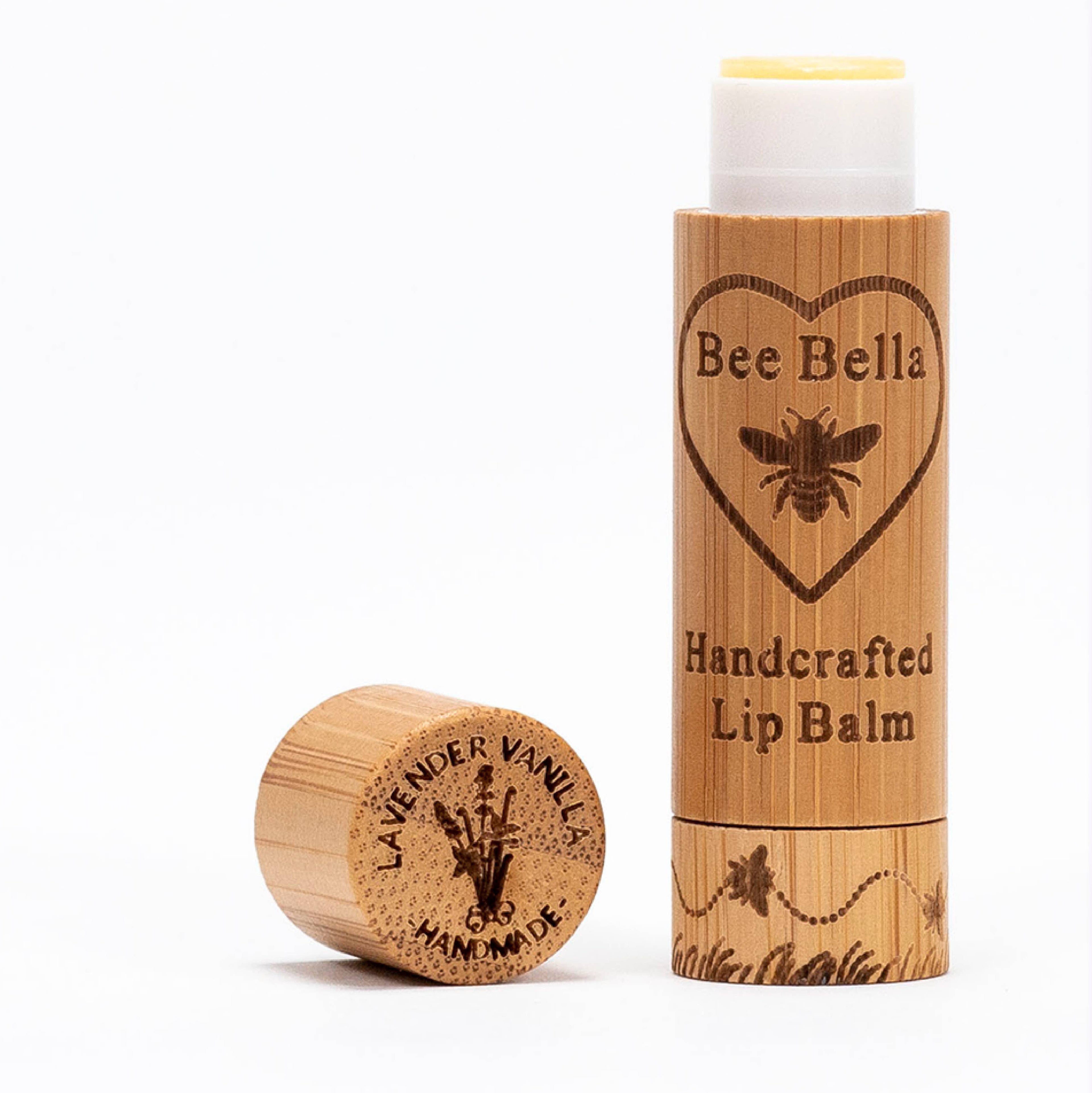 A bamboo tube of Lavender Vanilla Lip Balm stands upright with its cap off beside it. Both are engraved with bees and flowers and feature soothing Bulgarian lavender oil.