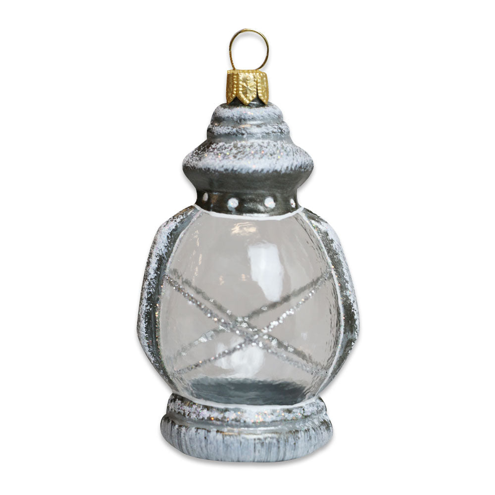 The Lantern Ornament is a hand-painted glass piece with vintage-inspired silver and gray details, glitter accents, and a gold loop.