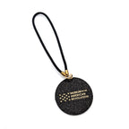 The Star Bag Charm is a round black keychain with gold “Museum of the American Revolution” text and stars, attached to a black looped strap with a gold clasp. Shown on a white background.