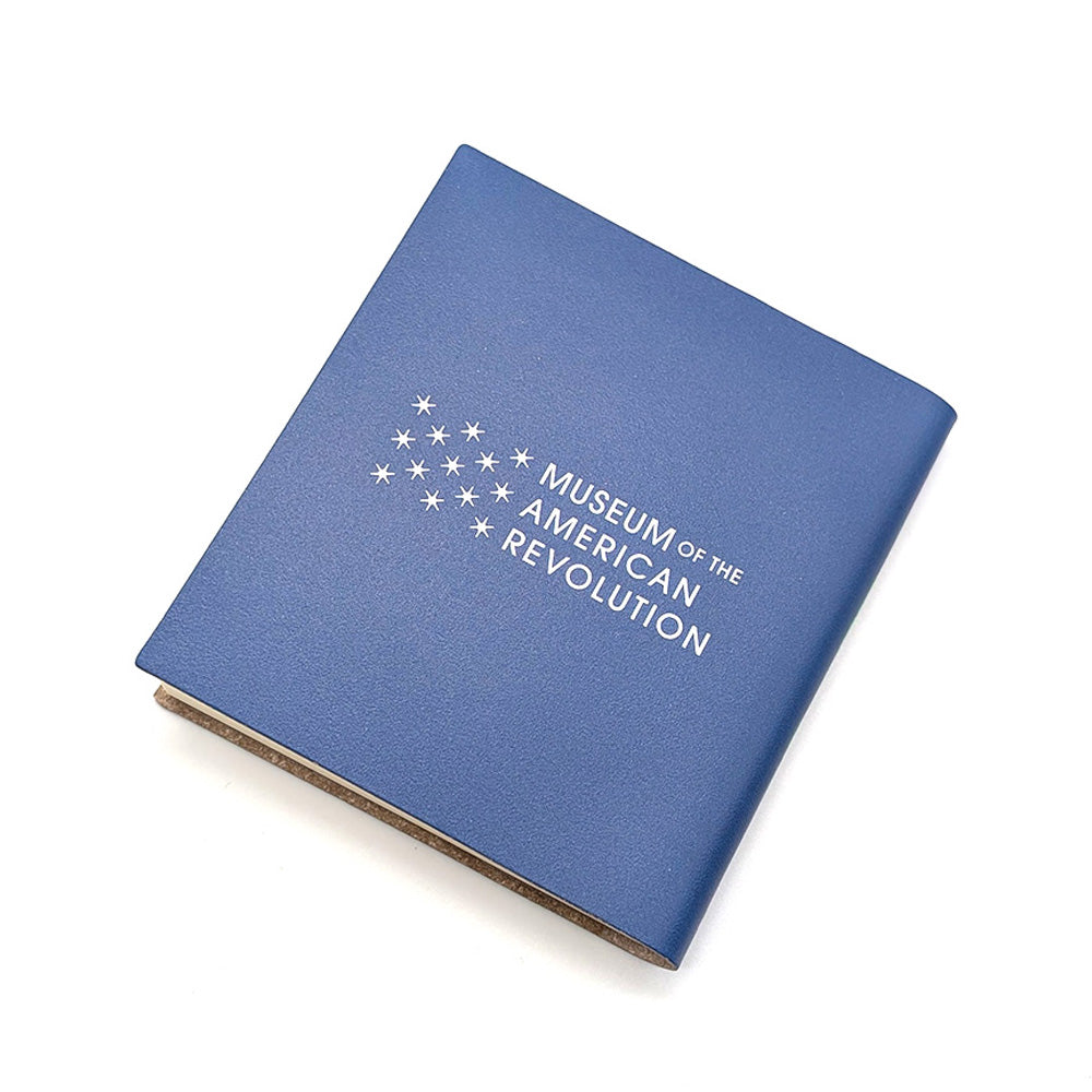 The Declaration Quote Journal is a blue compact notebook with "Museum of the American Revolution" and a white star design on the cover. Shown slightly open against a white background.