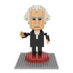 The George Washington Mini Blocks set features a LEGO-style figure with white hair and a black suit on a gray and red baseplate with a nameplate. With 323 pieces, it's perfect for collectors. The background is white.