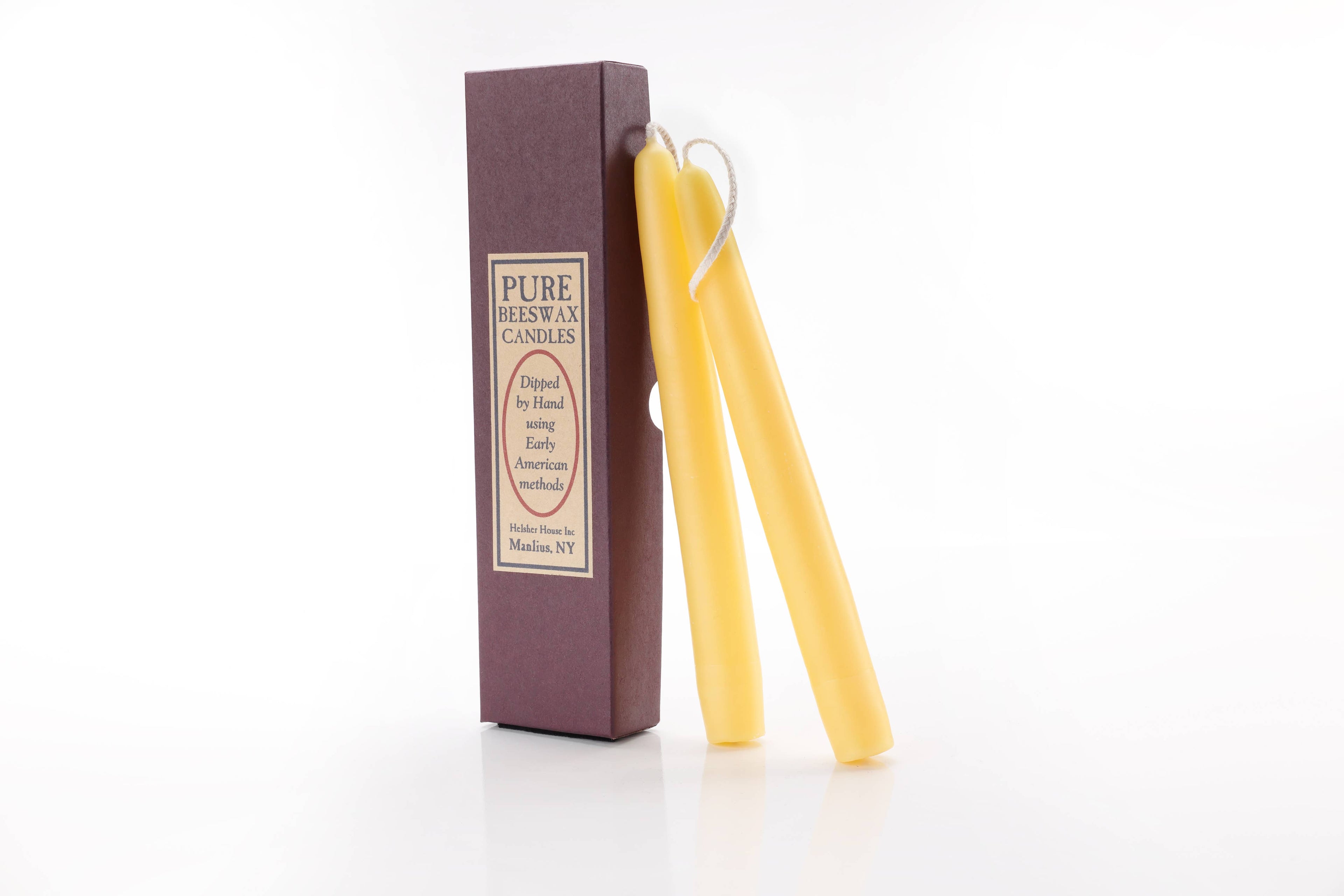 Two hand-dipped Beeswax Taper Candles rest against a brown box labeled “Beeswax Taper Candle.” The cream label emphasizes their natural purity, presented on a clean white background.