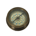 The Antiqued Solid Brass Compass features a white face with colored directional markings and decorative details. Its needle points north against a plain white background, evoking vintage charm.