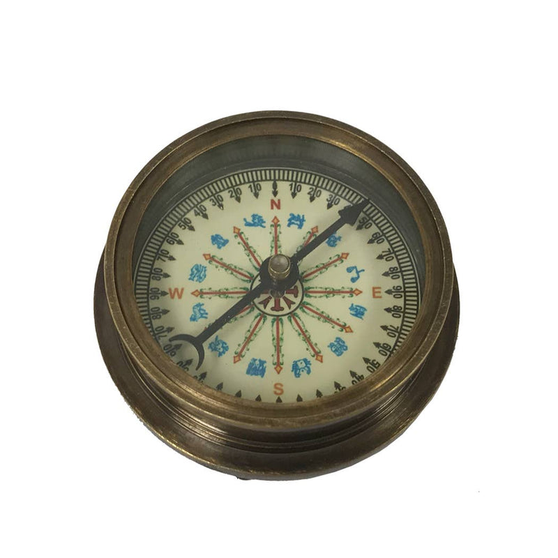 The Antiqued Solid Brass Compass features a white face with colored directional markings and decorative details. Its needle points north against a plain white background, evoking vintage charm.