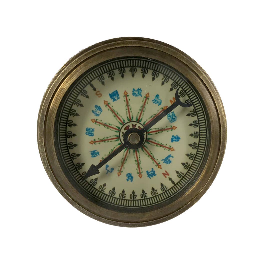 The Antiqued Solid Brass Compass features ornate detailing, directional points, decorative symbols on the face, and two black needles pointing in different directions.