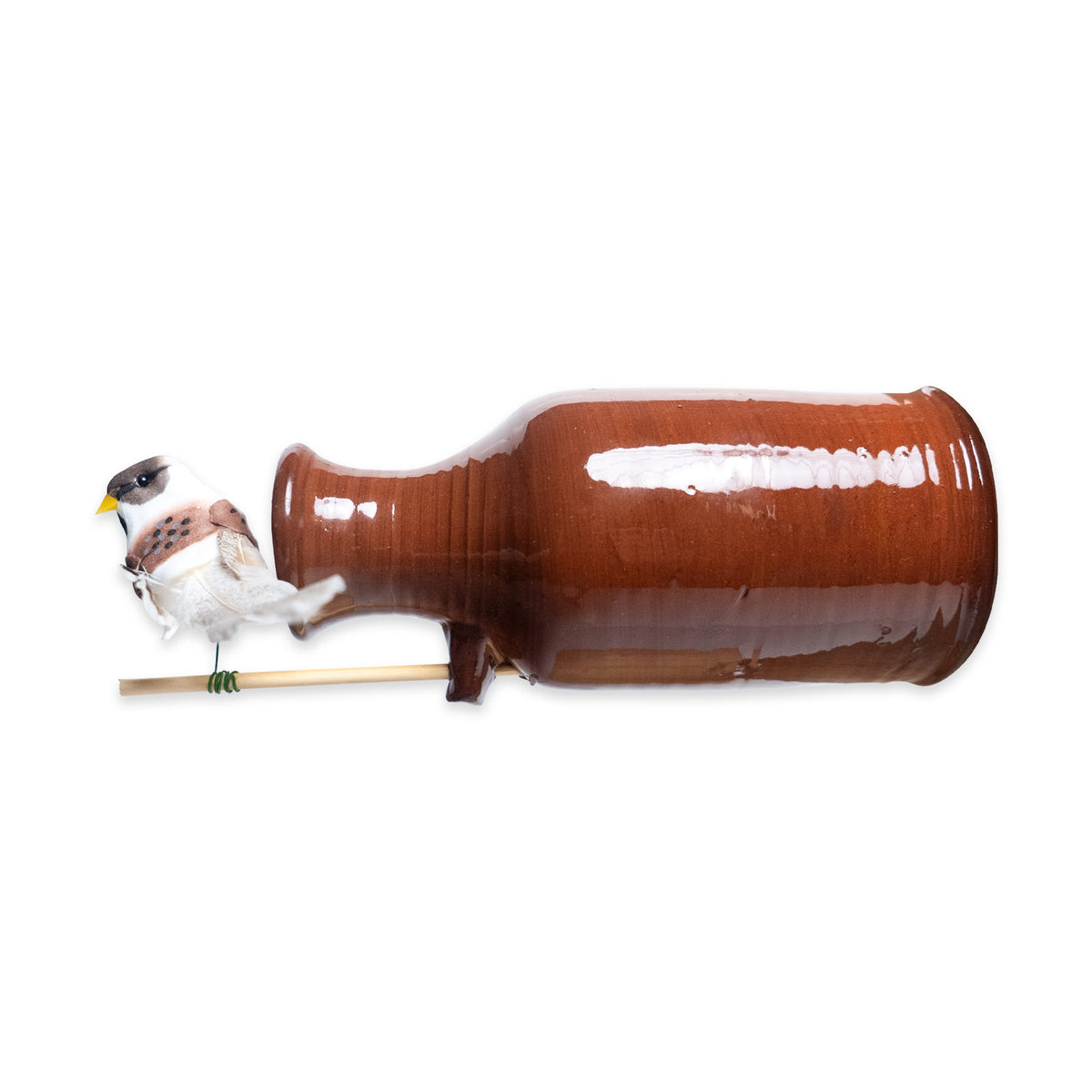 A Bird Bottle made of earthenware is shown lying on its side against a white background, with a small bird toy attached to a wooden stick inserted into its spout.