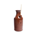 A Bird Bottle, crafted from brown ceramic and featuring a small spout with a hole near the middle that holds two thin wooden sticks, is displayed against a white background.