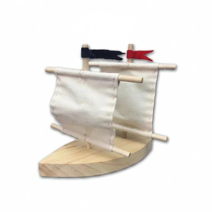 The Boat Kit includes a precut wooden hull, two carefully sewn white fabric sails, and two flags—black and red. This minimalist toy sailboat model is shown on a white background.