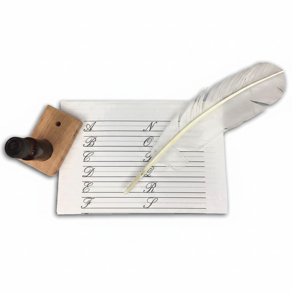 A white feather quill rests on penmanship practice paper beside an ink bottle in a wooden stand—an elegant set included in the Calligraphy Kit.