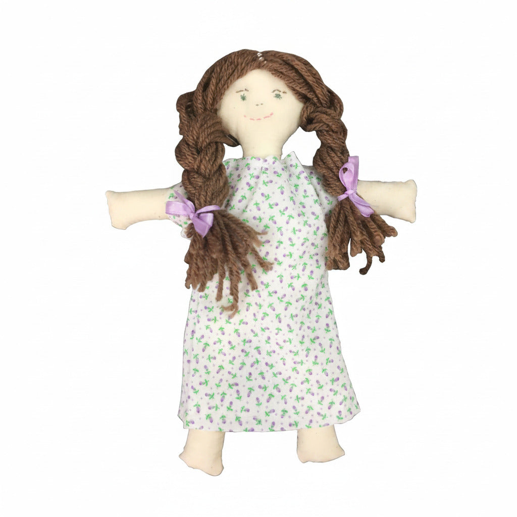 The Colonial Doll Kit lets you make a handmade cloth doll with brown yarn braids tied in purple ribbons and a white dress with a green floral print—a charming choice for history lovers and craft enthusiasts.