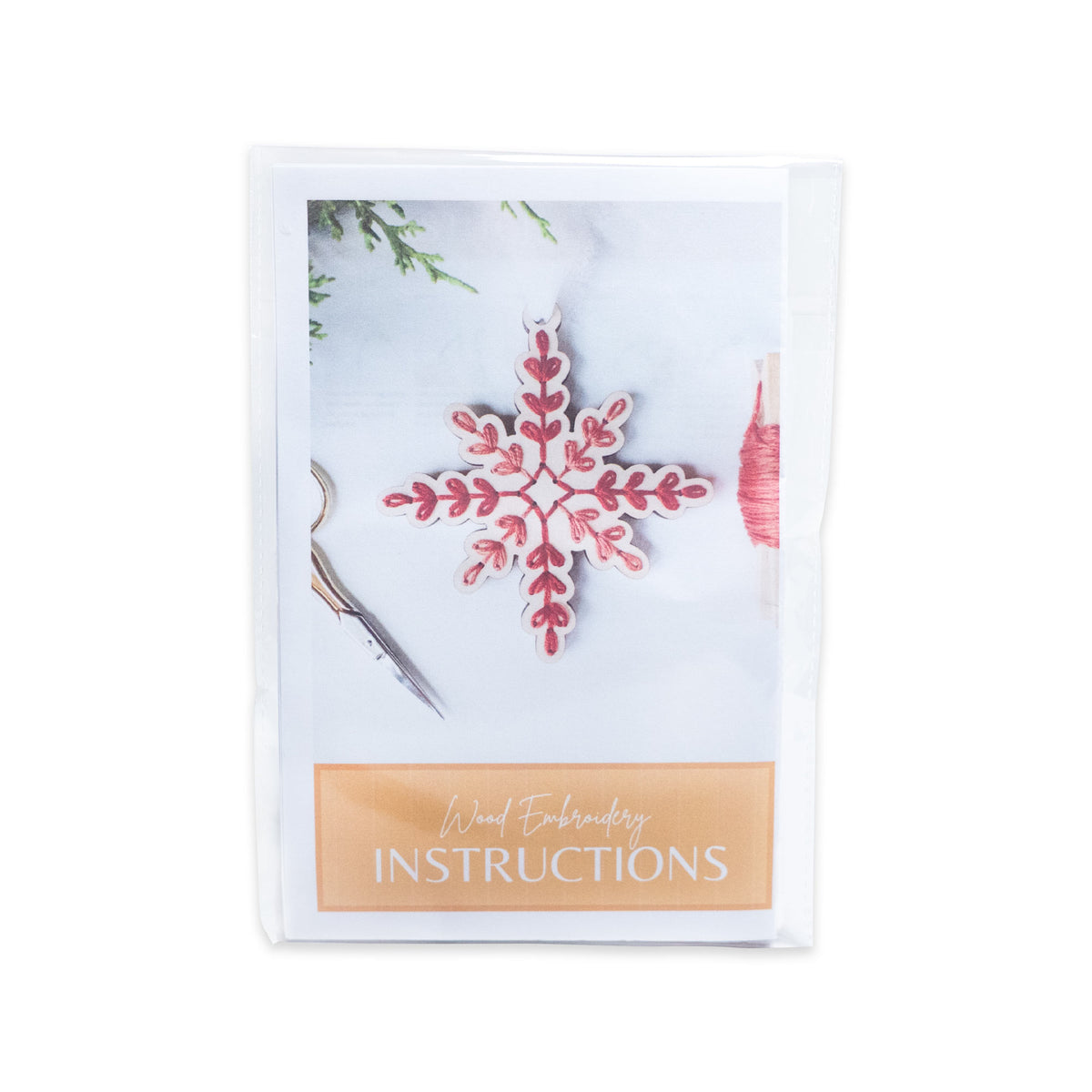Snowflake Ornament Embroidery Kit packaging showing a wooden snowflake ornament stitched with red thread and printed instructions at the bottom.