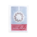 Pine Wreath Ornament Embroidery Kit in a clear plastic sleeve, showing a circular wood ornament with an embroidered wreath design above the text Wood Embroidery INSTRUCTIONS.