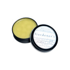 An open tin of yellow Gardener’s Hand Salve next to its lid.