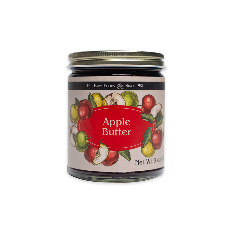 A glass jar of no sugar added Apple Butter with a label featuring illustrations of apples and the text Tait Farm Foods and Net Wt 9 oz.