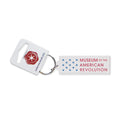 The Acrylic Museum Keychain is a rectangular acrylic accessory featuring the Museum of the American Revolution and blue stars, attached to a white tag with a red emblem and the website amrevmuseum.org—making it an ideal collectible gift for history enthusiasts.