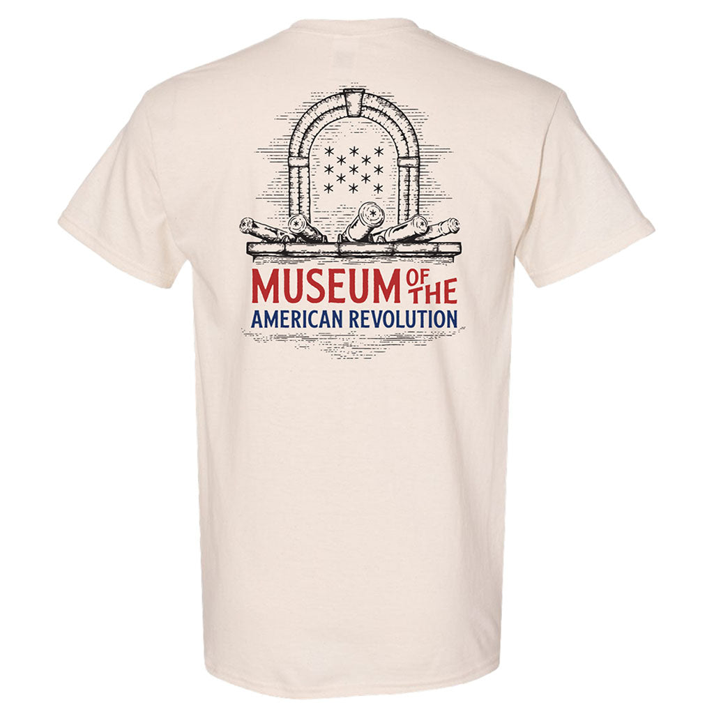 The Museum T-Shirt, Short Sleeve, is a beige tee with a sketch of an arch, cannons, and stars above "Museum of the American Revolution" in bold blue and red text on the back.