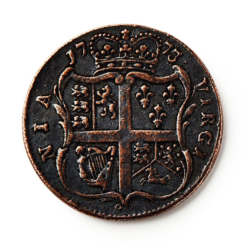 A 1773 Virginia Halfpenny with a crowned shield, heraldic symbols, and a cross is shown against a white background. The worn coin displays raised text and details and reflects British colonial currency design.