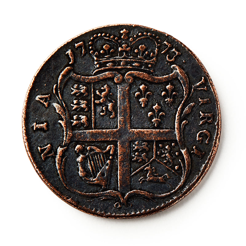 A 1773 Virginia Halfpenny with a crowned shield, heraldic symbols, and a cross is shown against a white background. The worn coin displays raised text and details and reflects British colonial currency design.