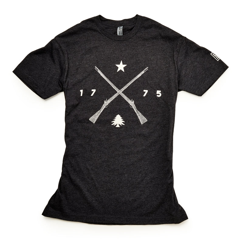 The 1775 Militia T-Shirt is a black tee with two crossed Pennsylvania muskets, a star above, 1775 on each side, and a small pine tree below—all in bold white print.