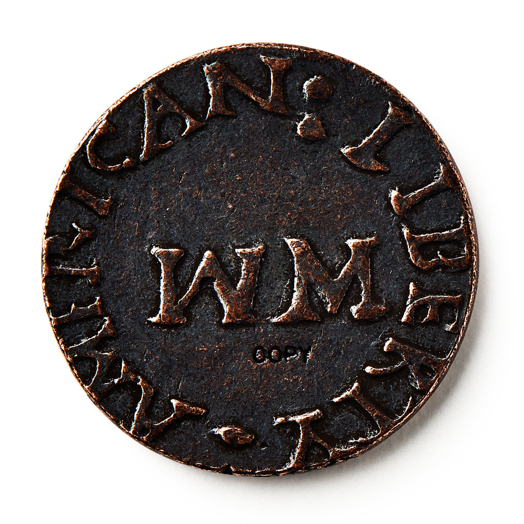 A close-up of a 1776 New Hampshire Halfpenny, an old colonial coin featuring large WM letters at its center and worn raised text around the edge that partially reads "AMERICAN LIBERTY.