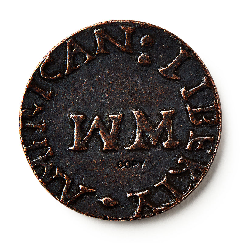 A close-up of a 1776 New Hampshire Halfpenny, an old colonial coin featuring large WM letters at its center and worn raised text around the edge that partially reads "AMERICAN LIBERTY.