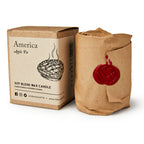 A boxed America Candle with an apple pie illustration sits next to a brown paper-wrapped candle sealed with red wax—perfect for adding a warm, inviting apple pie aroma to any space.