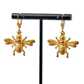 Bee Earrings featuring detailed gold bee designs with intricate wings and bodies, shown hanging from a black stand on a white background—ideal for fans of nature-inspired jewelry.