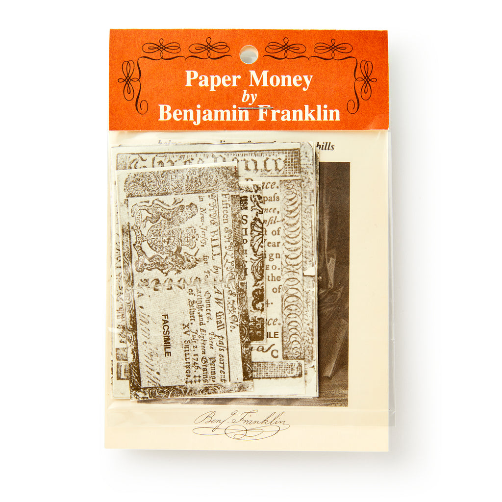 A plastic bag with an orange and white header labeled "Benjamin Franklin Paper Money" holds colonial currency replicas and a black-and-white portrait.