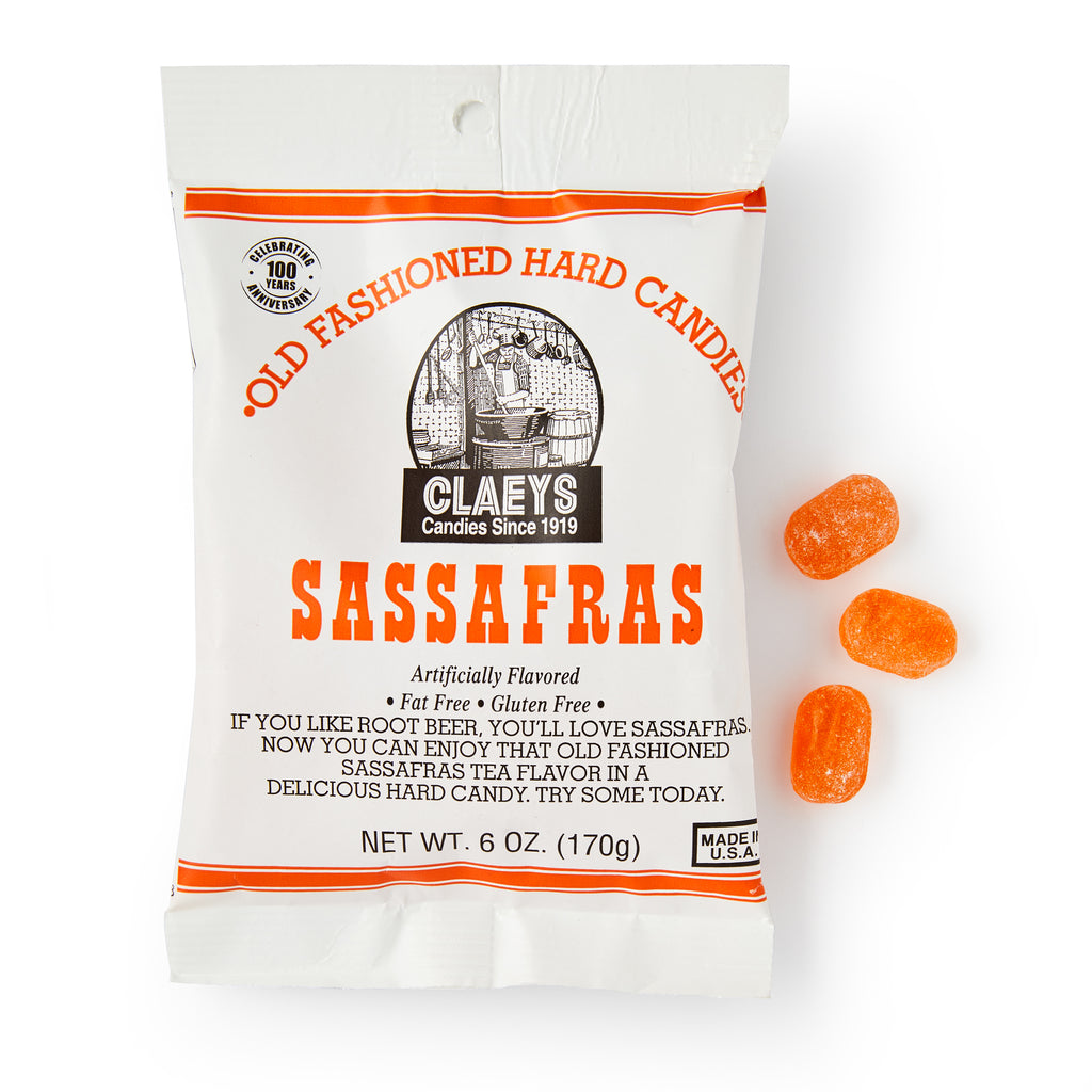 A white bag of Sassafras Old Fashioned Hard Candies sits beside orange candies. Vintage-style packaging features nostalgic black and orange text and graphics.