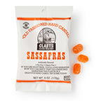 A white bag of Sassafras Old Fashioned Hard Candies sits beside orange candies. Vintage-style packaging features nostalgic black and orange text and graphics.