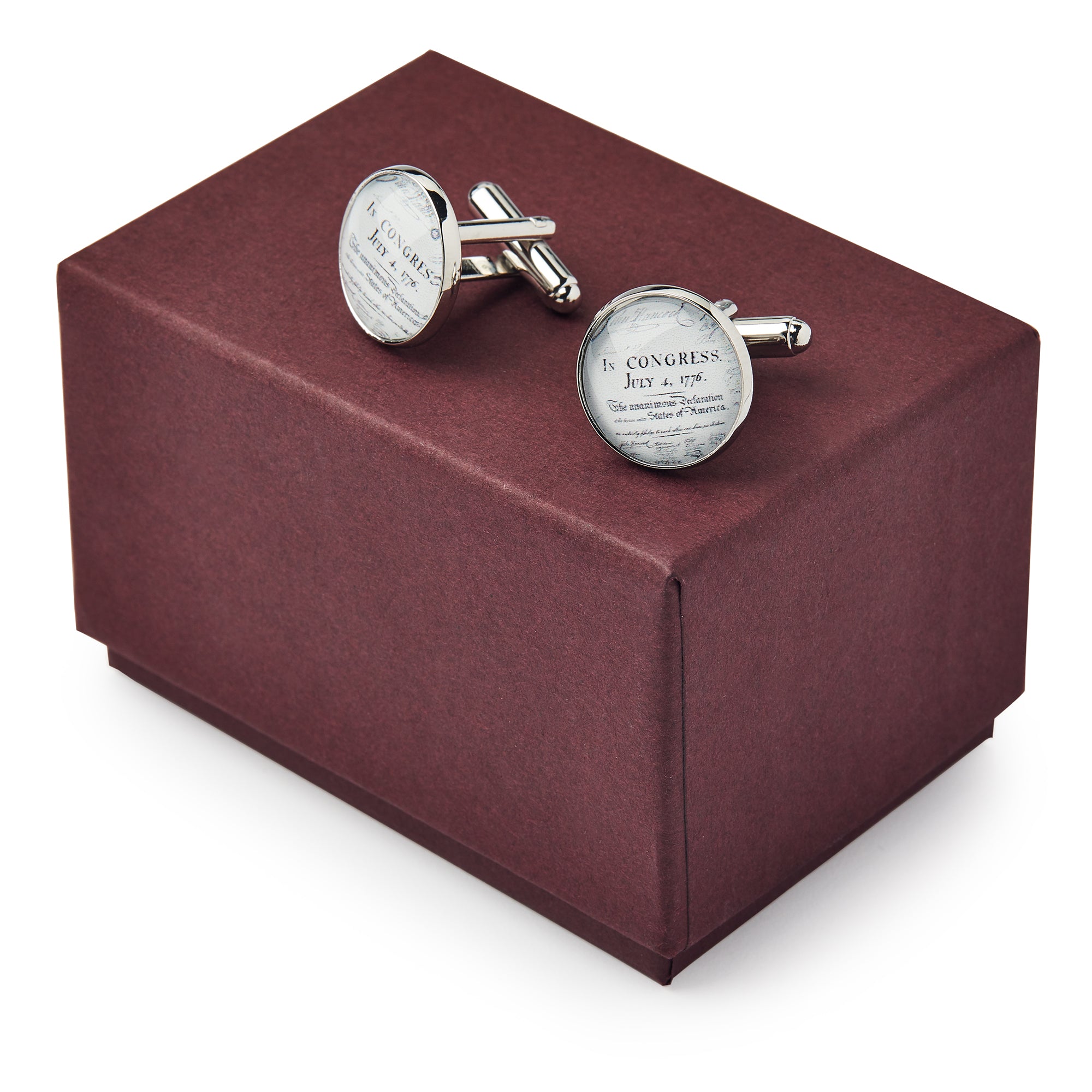 A pair of Declaration Cufflinks — round, silver, and engraved — rest on a closed maroon gift box.