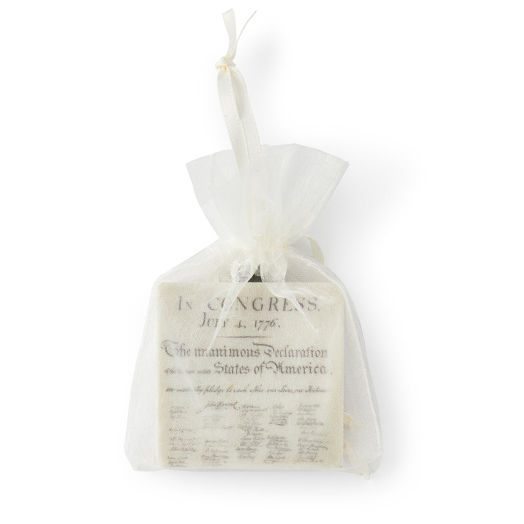 A small white mesh gift bag containing the Declaration of Independence Ornament—a stone ornamment printed with the historic text and signatures.