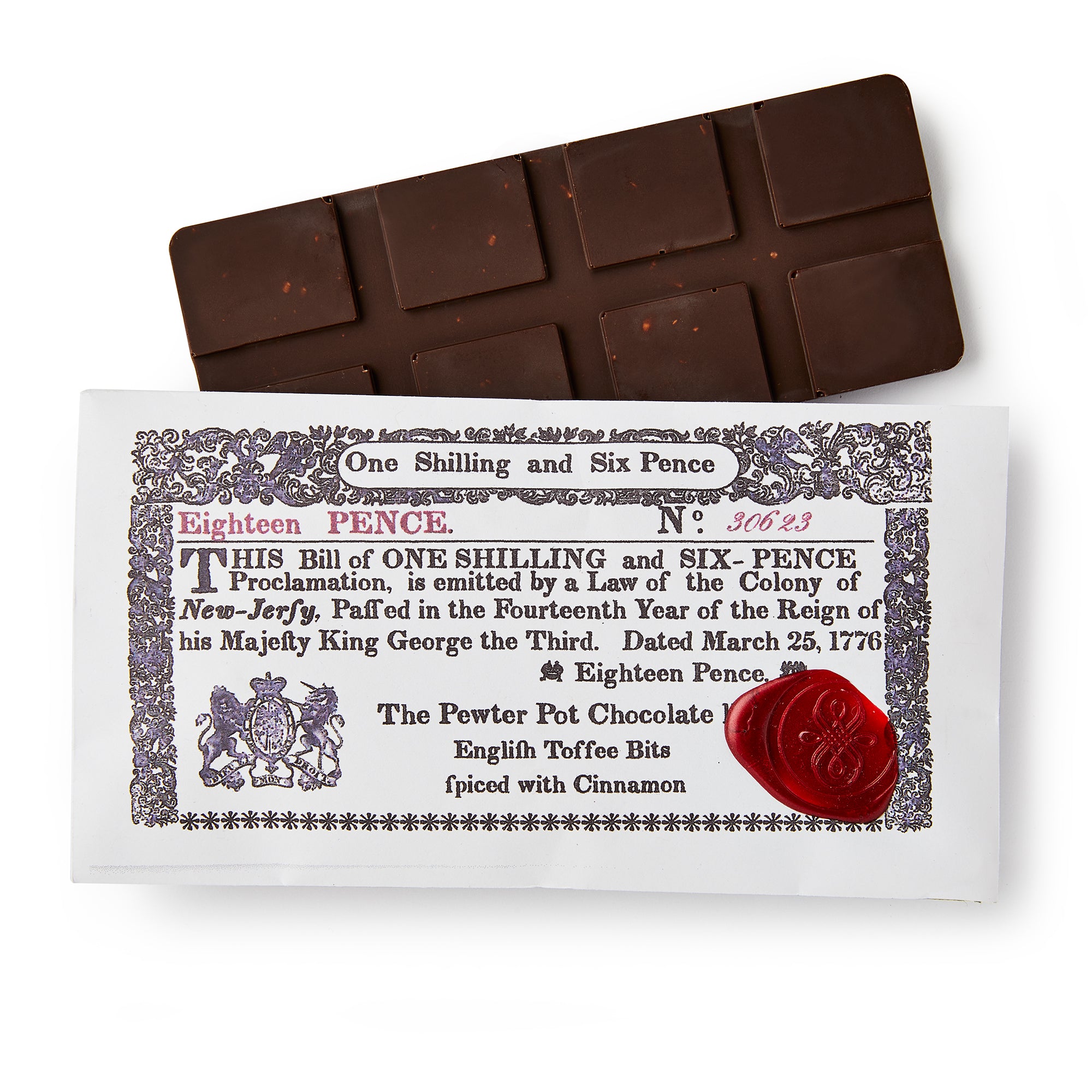 The New Jersey Chocolate Bar rests on an old currency-style wrapper marked "One Shilling and Six Pence," featuring vintage text, a red wax seal, and describing cinnamon-spiced English toffee dark chocolate.