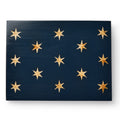 The George Washington Standard Wooden Flag displays a rectangular dark blue surface with thirteen gold stars arranged in uneven rows, inspired by Revolutionary War flag designs.