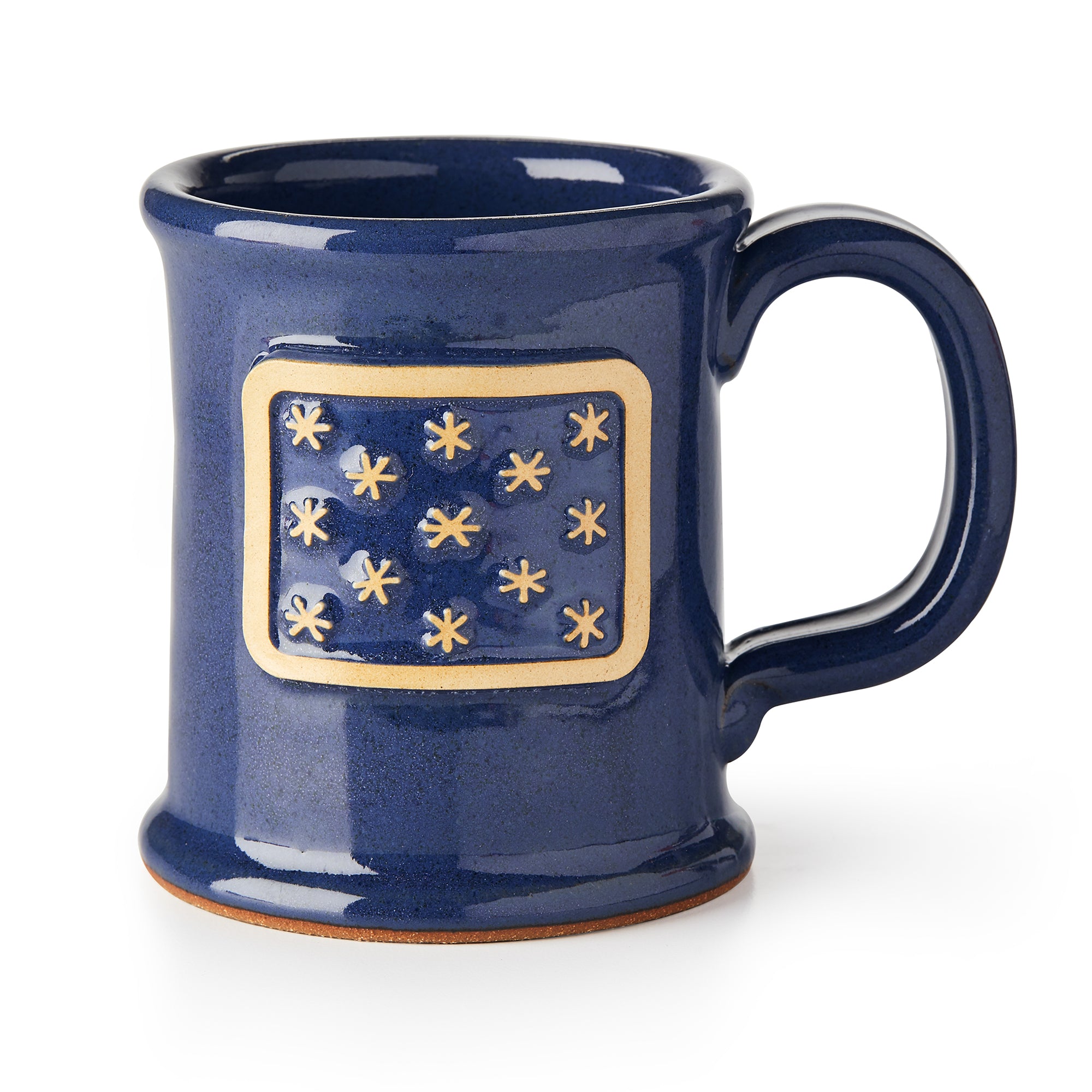 The George Washington Standard Mug is a dark blue stoneware mug with a rectangular tan patch displaying 13 raised star-like shapes inspired by the George Washington flag. It features a large rounded handle and slightly flared rim.