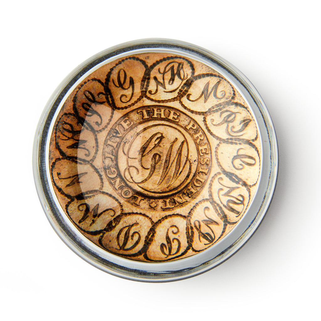 The GW Linked States Paperweight is round with an ornate "GW" monogram in the center, encircled by "Long live the president" in decorative script, and is shown from above on a white background.