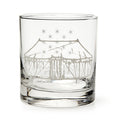 The George Washington Tent Whiskey Glass is a clear tumbler etched with a large circus tent and stars, inspired by the original whiskey glass. Displayed empty against a white background.