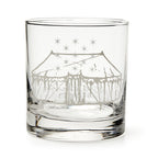 The George Washington Tent Whiskey Glass is a clear tumbler etched with a large circus tent and stars, inspired by the original whiskey glass. Displayed empty against a white background.