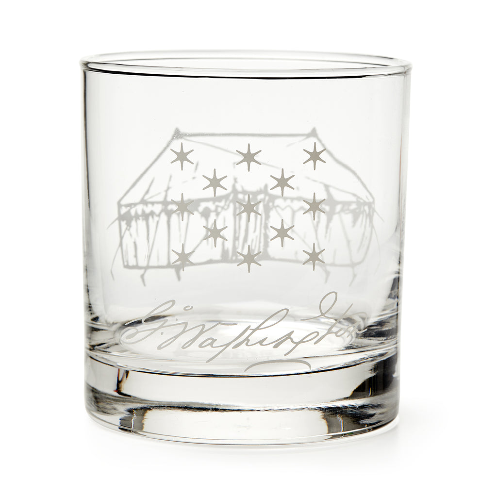 The George Washington Tent Whiskey Glass features a clear glass design engraved with a starry tent and cursive signature, reminiscent of classic Washington whiskey glasses, displayed empty against a white background.