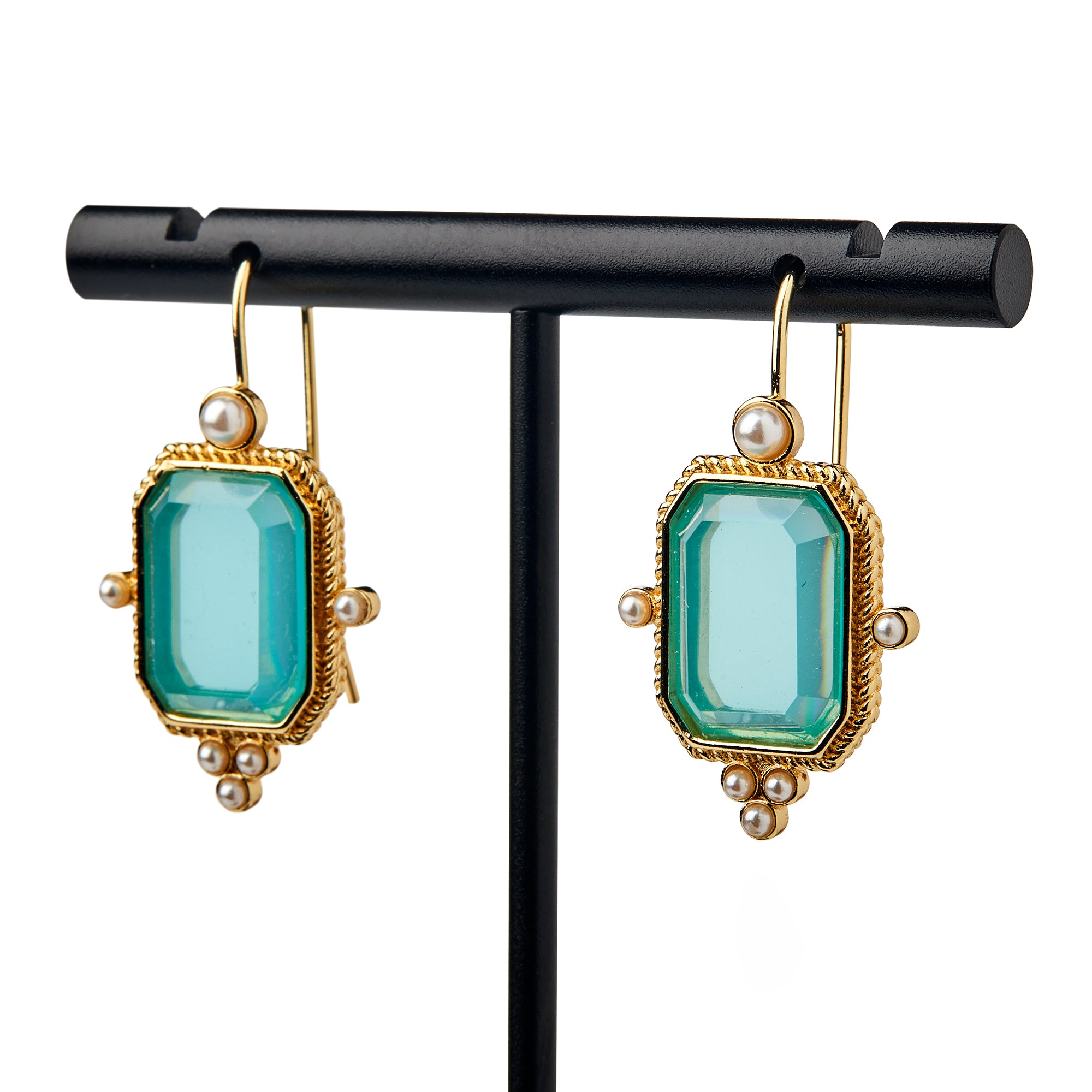 The Glass Intaglio and Pearl Earrings, Teal, feature gold drop design with rectangular teal glass stones and small white pearls on gold-plated earwires, reflecting colonial-era craftsmanship, displayed on a black stand against a white backdrop.