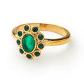 The Green Crystal Forget-Me-Not Ring is a gold-plated stainless steel piece with an oval green gemstone center, accented by a floral halo of smaller green stones, inspired by forget-me-not flowers, displayed on a white background.