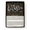 Black Snake Earrings, shaped like snakes with white detailing, are shown in a box featuring a segmented snake and text on the historic “Join, or Die” symbol and colonial unity from the American Revolution.