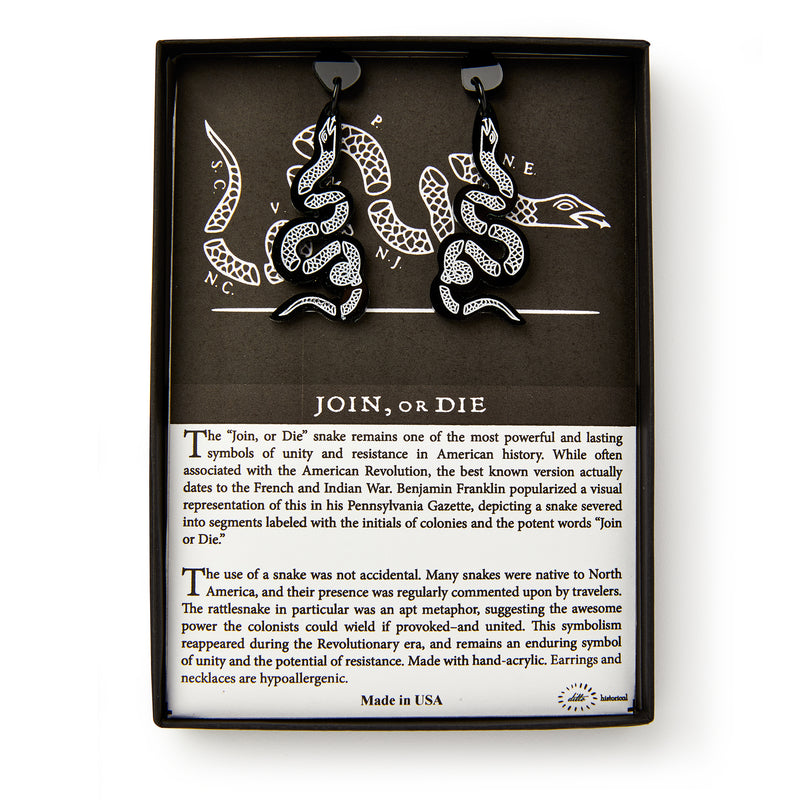 Black Snake Earrings, shaped like snakes with white detailing, are shown in a box featuring a segmented snake and text on the historic “Join, or Die” symbol and colonial unity from the American Revolution.