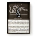 The Black Snake Necklace features a black and white snake pendant on a chain, presented in a box. The background shows the iconic Join or Die snake illustration with text explaining its Revolutionary-era jewelry significance.