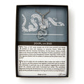 A boxed jewelry set, the Clear Snake Necklace, displays a silver pendant shaped like the iconic segmented snake with directional letters in the background and a description emphasizing its historical message of unity and resistance.