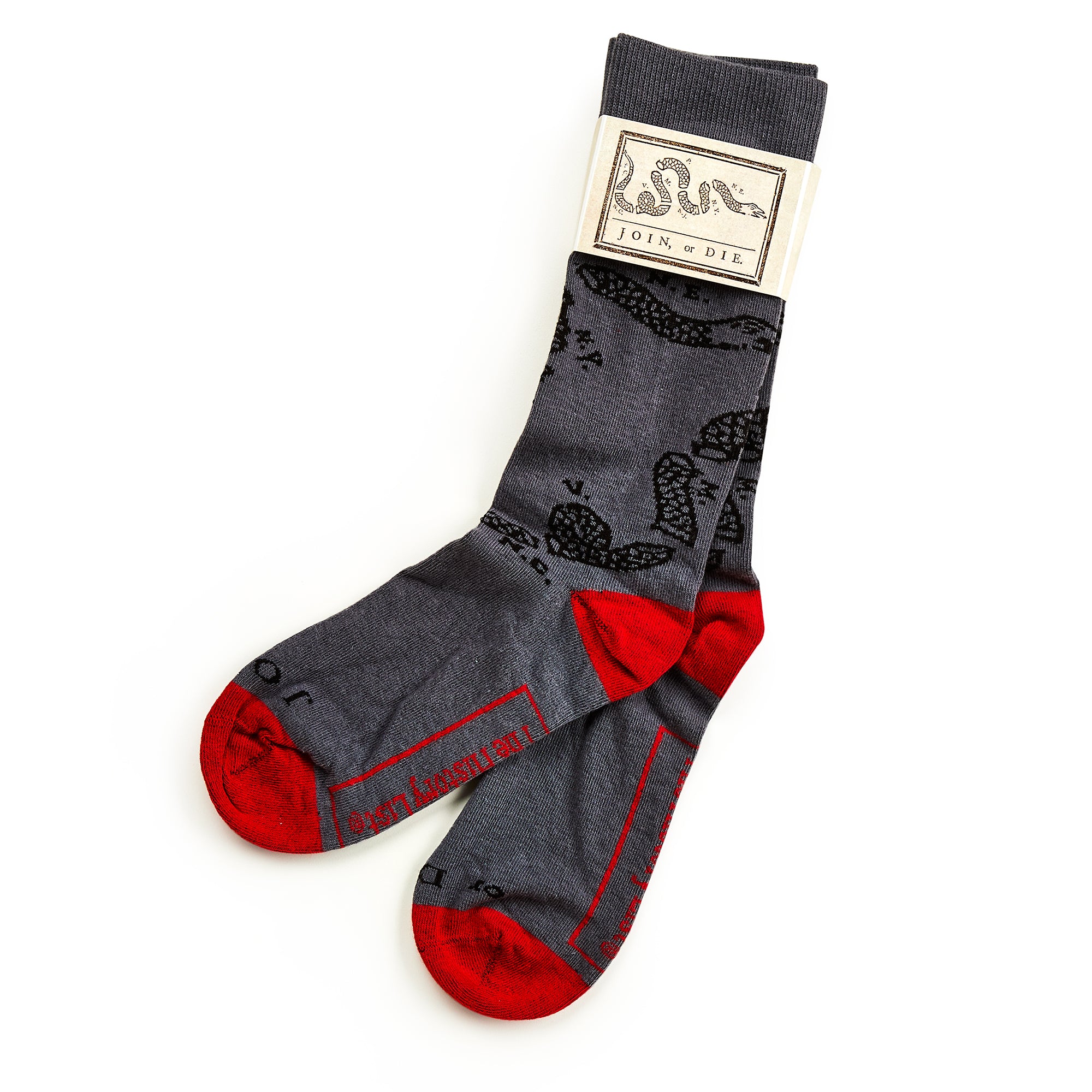 Join or Die Socks feature gray fabric with red toes and heels, plus a black snake inspired by Benjamin Franklin's illustration. Packaged with a tag displaying the iconic slogan and artwork.