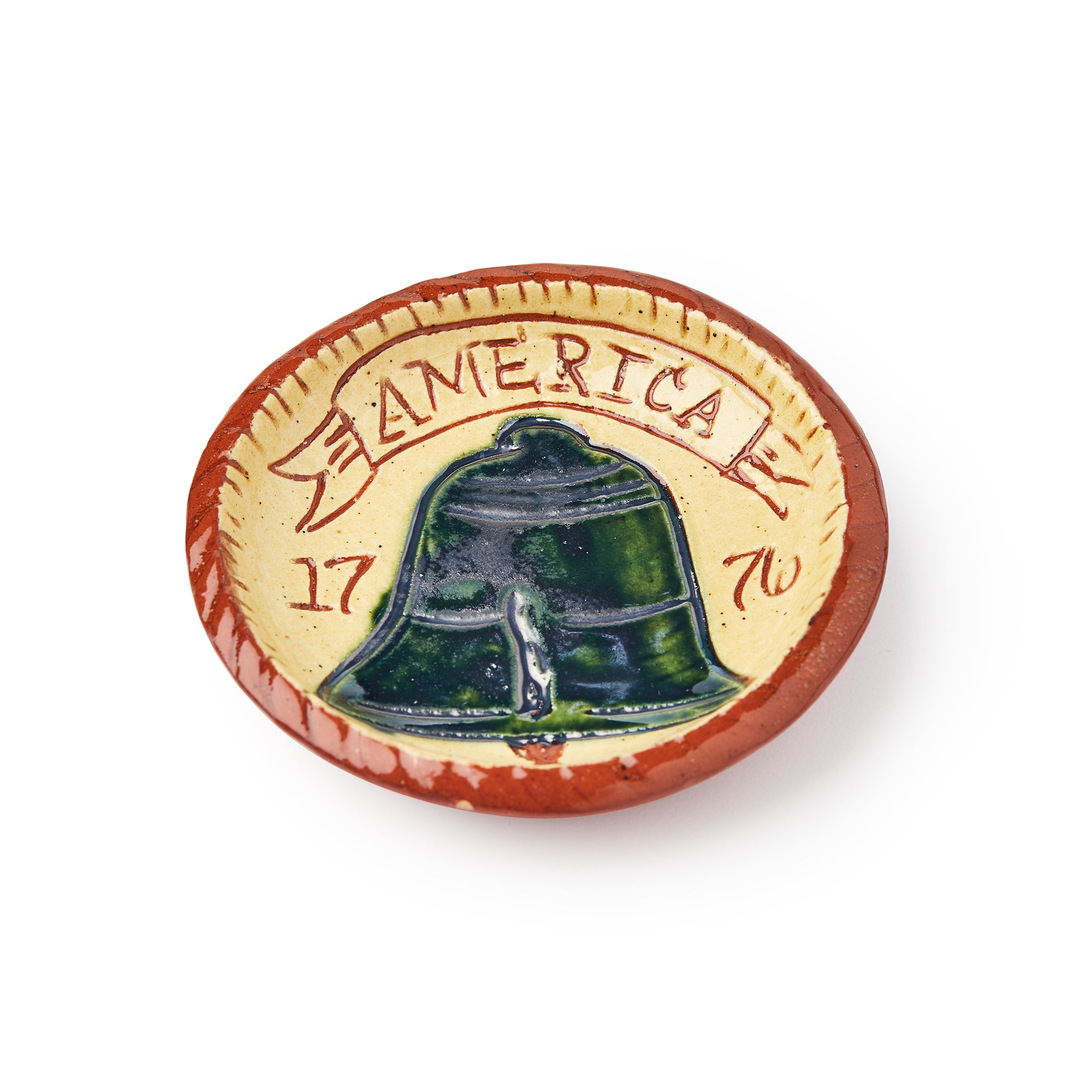 The Liberty Bell Plate, 3" features a raised bell image with "AMERICA" and "1776" above it on a tan background, accented by a reddish-brown rim inspired by classic redware pottery and colonial craftsmanship.