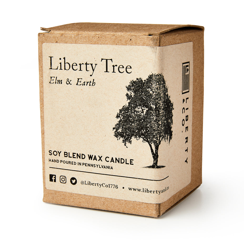 A brown cardboard box labeled Liberty Tree Candle features a black tree illustration and social media info, highlighting the hand-poured elm and earth soy blend scent made in Pennsylvania.